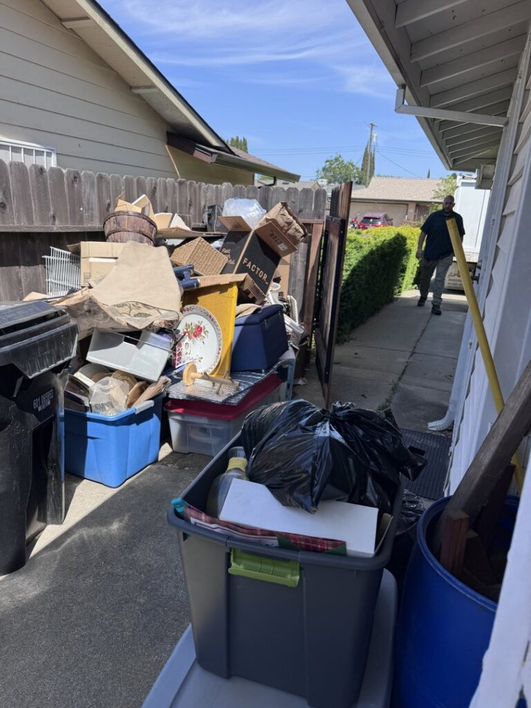 A large pile of household junk and boxes in a narrow side yard, ready for removal by Sac Junk in Rancho Cordova, CA
