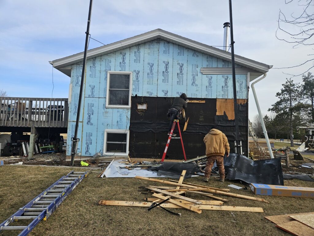 Workers installing siding on a house, with blue insulation wrap visible, by First Contracting Group in Rockford, IL.