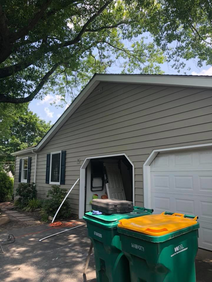Siding installation in progress on the side of a house, with tools visible inside an open garage, by Quality Care Home Improvements in Hamilton, NJ.