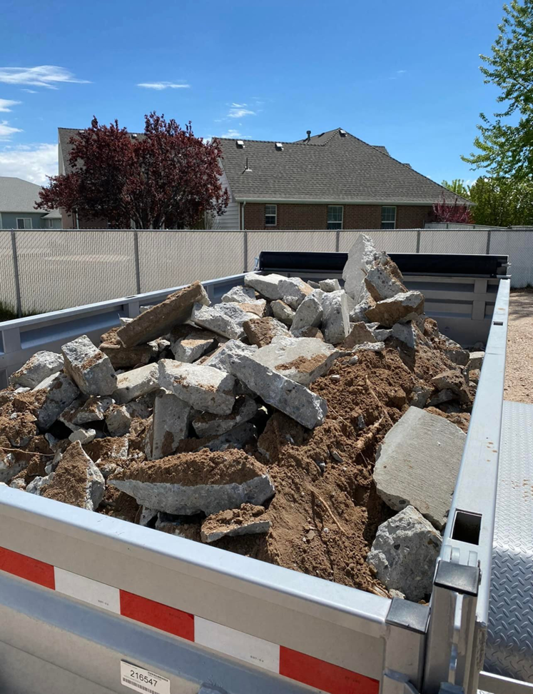 A silver dump trailer filled with concrete debris and dirt, ready for removal by S&J Rental and Removal in Ogden, UT.