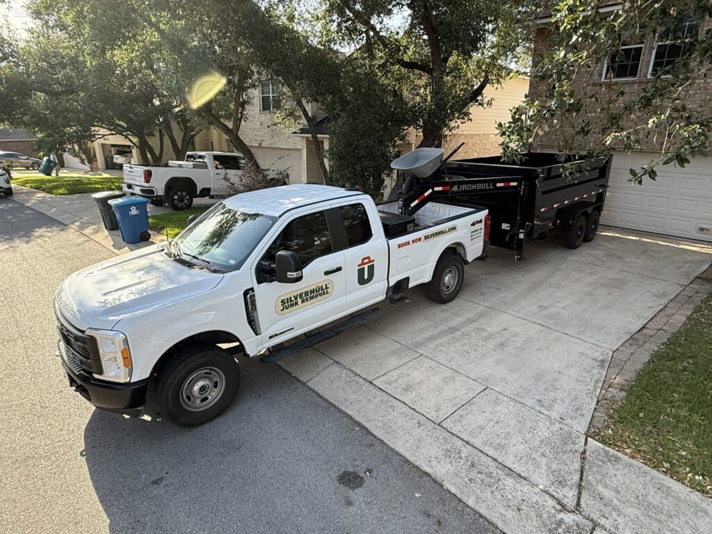 A Silverhull Junk Removal branded pickup truck with a dump trailer parked in a driveway in San Antonio, TX