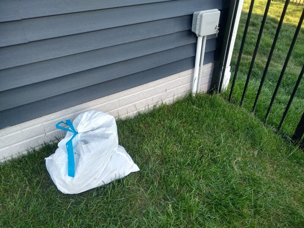 A single white bag of collected pet waste, tied with a blue ribbon, placed on a green lawn after a cleanup by They Poop We Scoop in Lewes, DE.