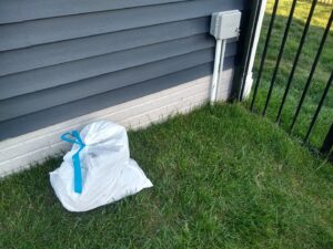 A single white bag of collected pet waste, tied with a blue ribbon, placed on a green lawn after a cleanup by They Poop We Scoop in Lewes, DE.