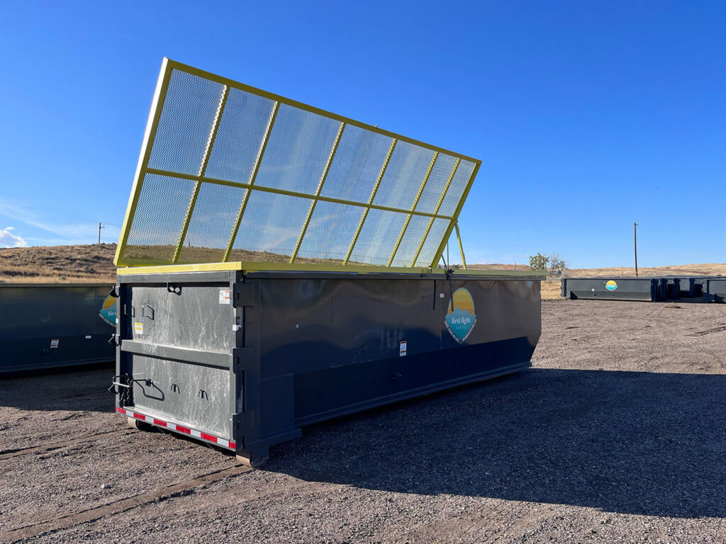A single roll-off dumpster with its yellow safety net open, provided by First Light Services Llc in Casper, WY.