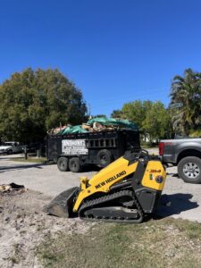 A yellow skid steer parked next to a dump trailer filled with junk for Anthony's Junk Removal & Delivery LLC in Cape Coral, FL.