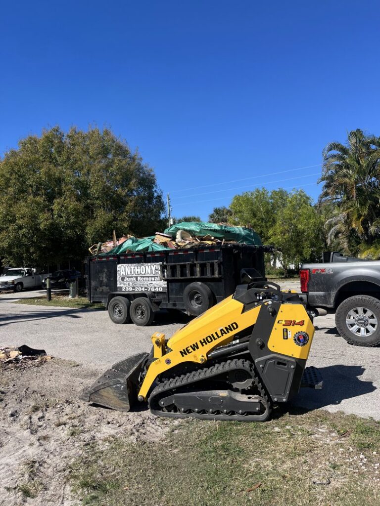 A yellow skid steer parked next to a dump trailer filled with junk for Anthony's Junk Removal & Delivery LLC in Cape Coral, FL.