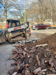 A Bobcat skid-steer loader next to a pile of brick and dirt debris, handled by Standard Dumpster LLC in Rock Hill, SC.
