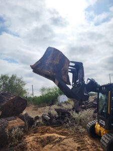 A skid steer with a grapple attachment lifting a large tree trunk section in San Antonio, TX, by Quicken Tree service.