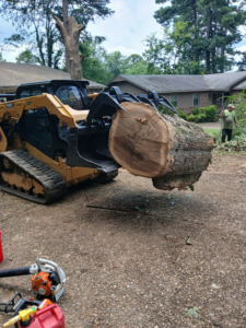 A skid steer lifting a large tree trunk section during a tree removal job by Monterroso tree service in Little Rock, AR.
