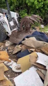 A skid-steer loader with a grapple attachment moving a pile of mixed construction debris for Junk Be Gone in Miami, FL.