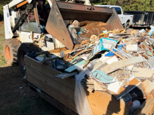 A skid steer efficiently loading a large pile of construction and household debris for JDog Junk Removal & Hauling in Concord, NC.