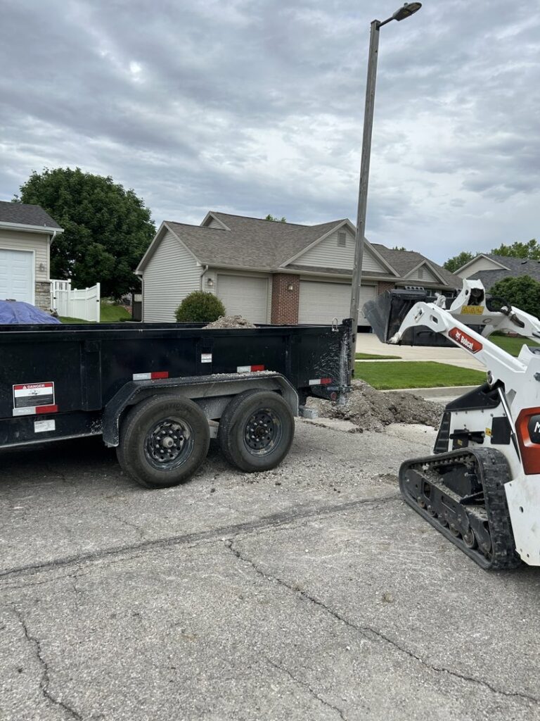 A skid steer loading debris into a dump trailer for Rosales Junk Removal in Des Moines, IA.