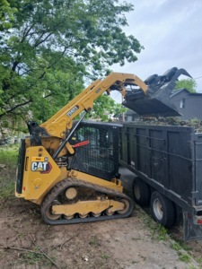 A skid steer loading tree branches and debris into a large dump trailer for Monterroso tree service in Little Rock, AR.