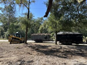 A skid steer loading yard debris into a trailer for junk removal by Big Skye Dumpsters in Jacksonville, FL.