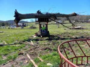 A skid steer moving a large fallen tree trunk during a cleanup operation by Ratliff Landscape and Tree Service LLC in Murfreesboro, TN