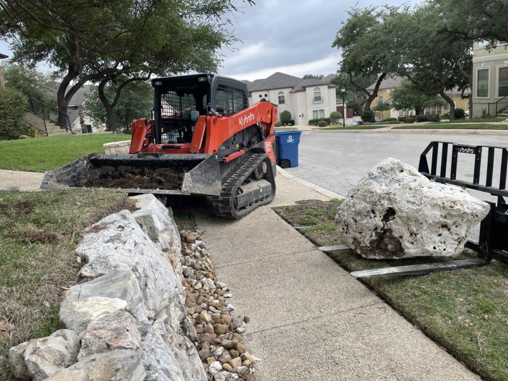 A skid steer moving a large rock for a landscaping project by R and R contractors in Rogers, AR.