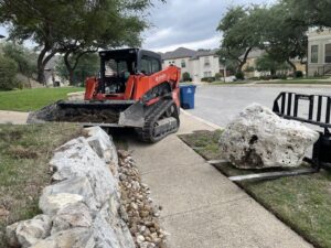 A skid steer moving a large rock for a landscaping project by R and R contractors in Rogers, AR.