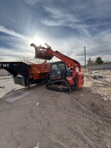 A skid steer with an attachment positioned next to a dumpster trailer for a junk removal job by Easy Load Disposal El Paso in El Paso, TX.