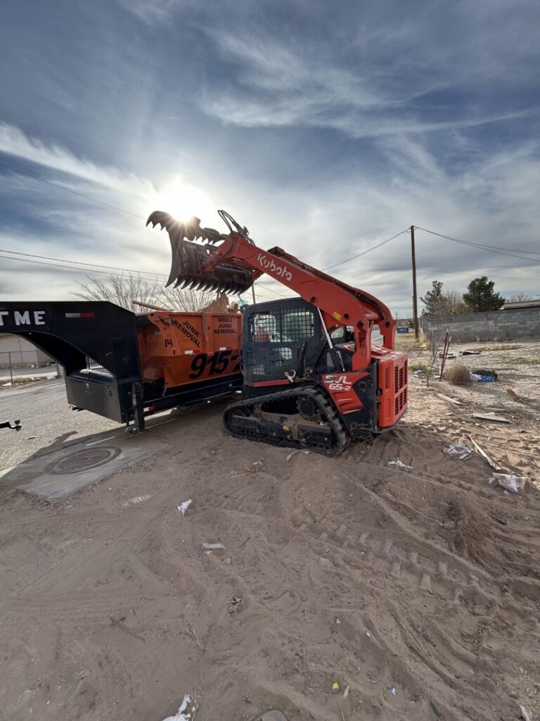A skid steer with an attachment positioned next to a dumpster trailer for a junk removal job by Easy Load Disposal El Paso in El Paso, TX.