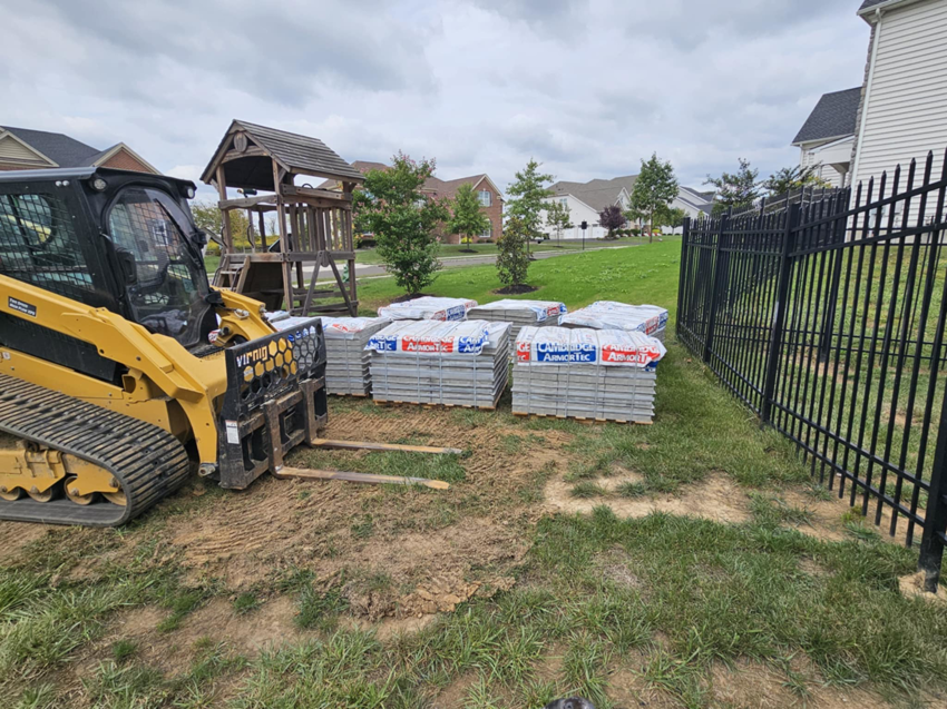 A skid steer and pallets of pavers on a job site for pool deck construction by Composite Pools USA in Newfield, NJ.