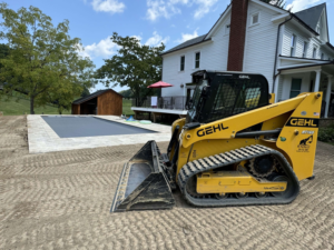 A skid steer on a prepared site next to a partially installed pool by Composite Pools USA in Newfield, NJ.