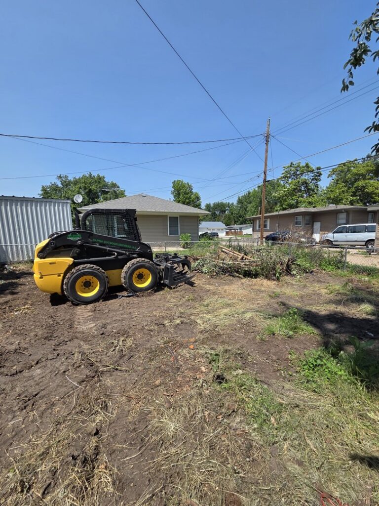 A skid steer with an attachment used for clearing tree branches and debris by Alpha Outdoor Services LLC in Kearney, NE.