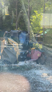A skid steer loader with a stump grinder attachment actively working on a tree stump for Farm Services in Scottown, OH.