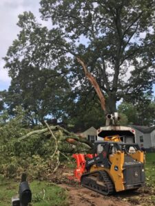A skid steer with a wood chipper attachment efficiently processing tree branches during a cleanup by Wallace Tree Service in Russellville, AL.