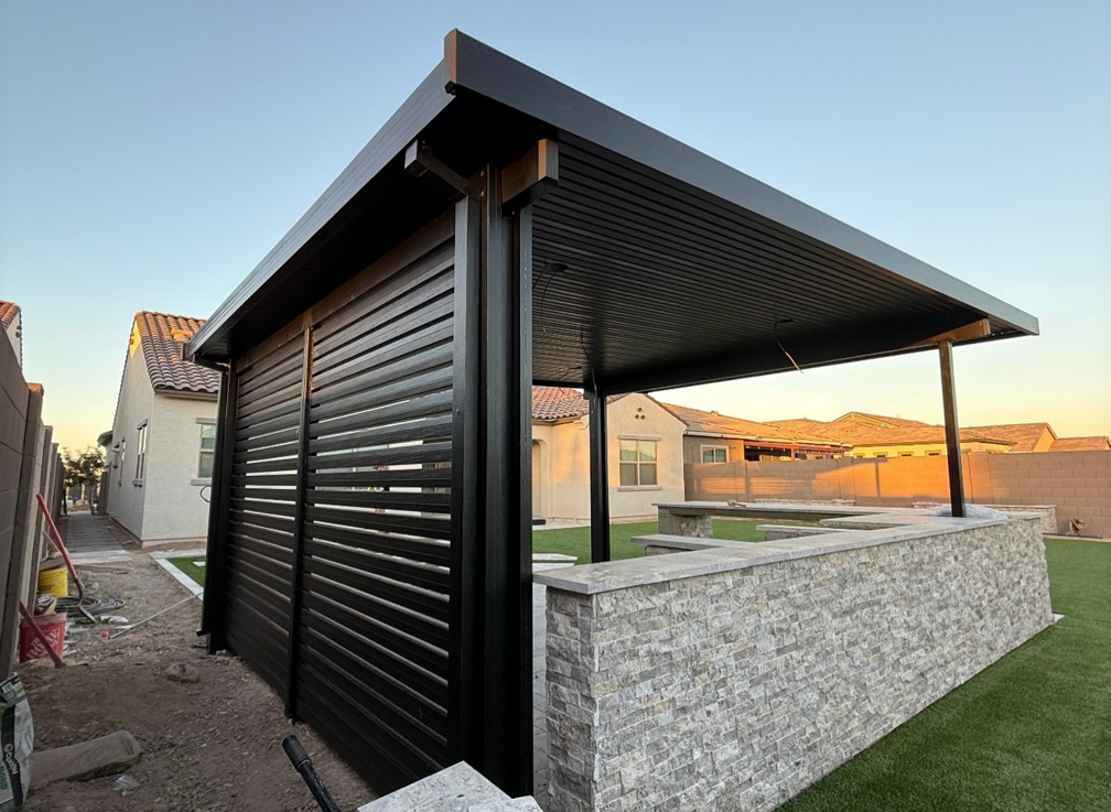 A side view of a black slatted patio cover and stone outdoor kitchen by Az Sun Covers in Glendale, AZ.