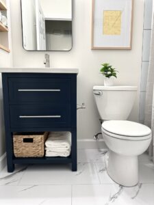 A small, renovated bathroom featuring a navy blue vanity, toilet, and white marble-look floor installed by Westrick Homes in St. Louis, MO.