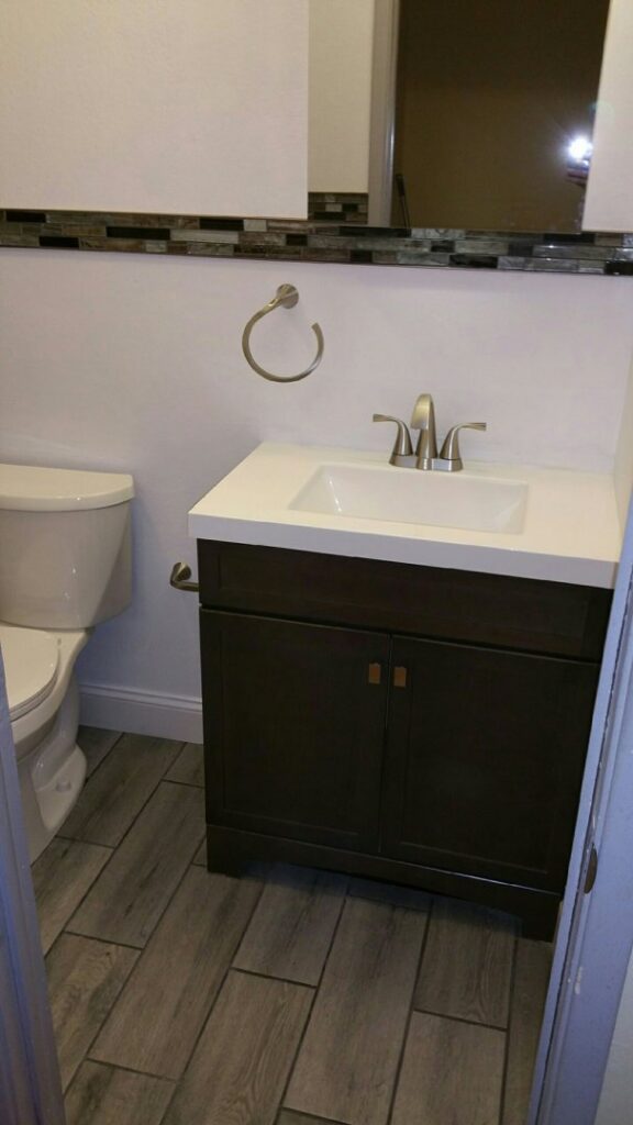 A small renovated bathroom with a new vanity, toilet, and wood-look tile flooring by The Foundation Guys in Lakewood, CO