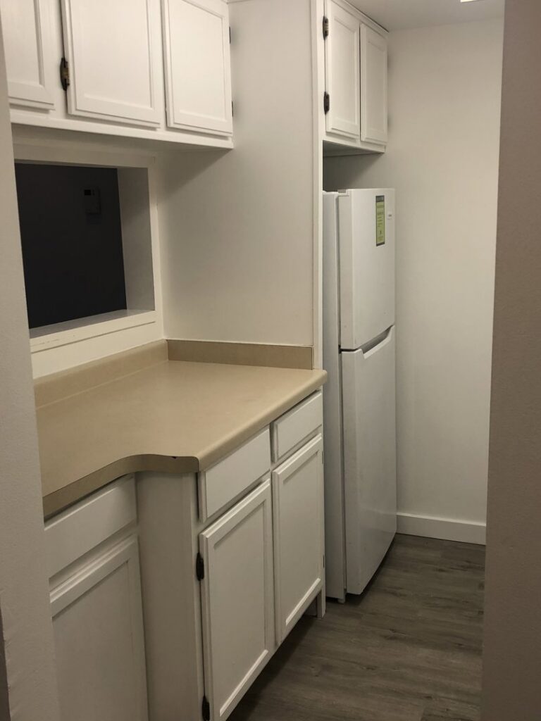 A compact kitchen or utility area with white cabinets and a refrigerator by RT Property Services in Allendale, MI