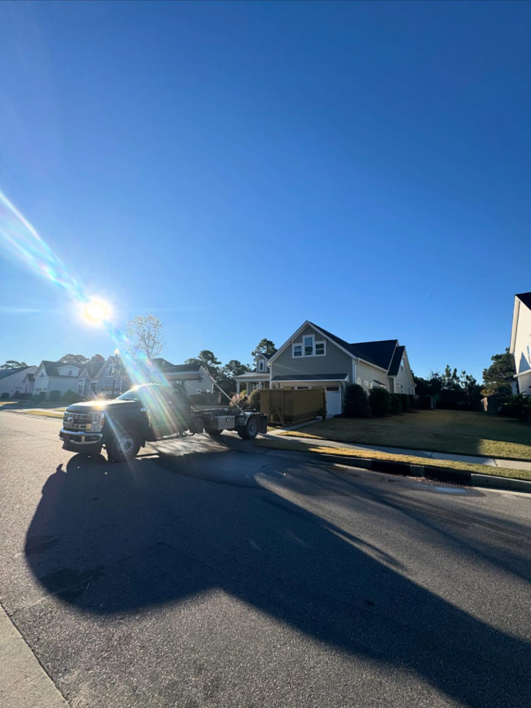A SmartDumps truck delivering a yellow roll-off dumpster to a residential neighborhood in Wilmington, NC.