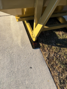 SmartDumps yellow dumpster with protective pads placed on the edge of a concrete driveway and grass in Wilmington, NC.