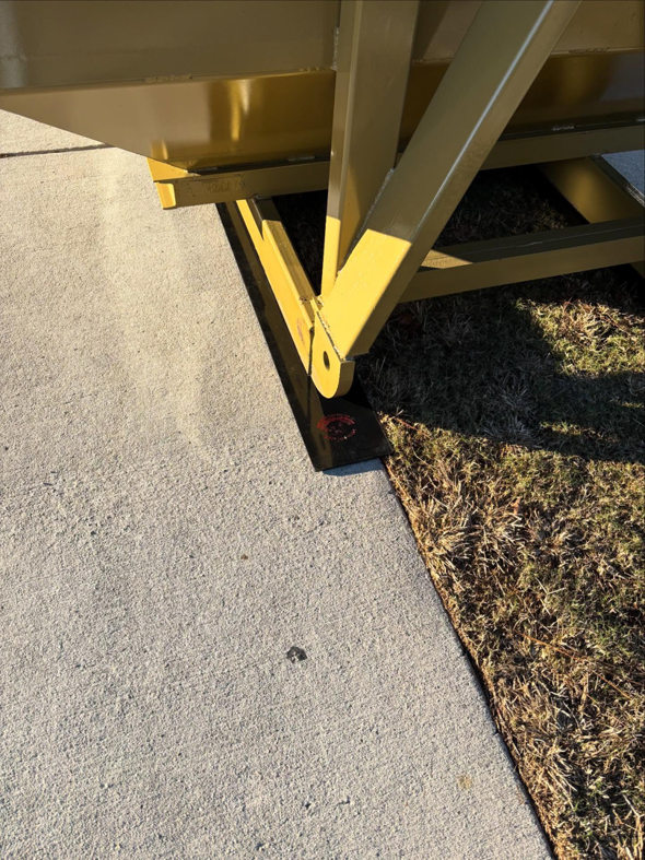SmartDumps yellow dumpster with protective pads placed on the edge of a concrete driveway and grass in Wilmington, NC.
