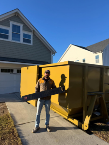 A SmartDumps employee standing in front of a yellow roll-off dumpster, holding a protective pad in Wilmington, NC.