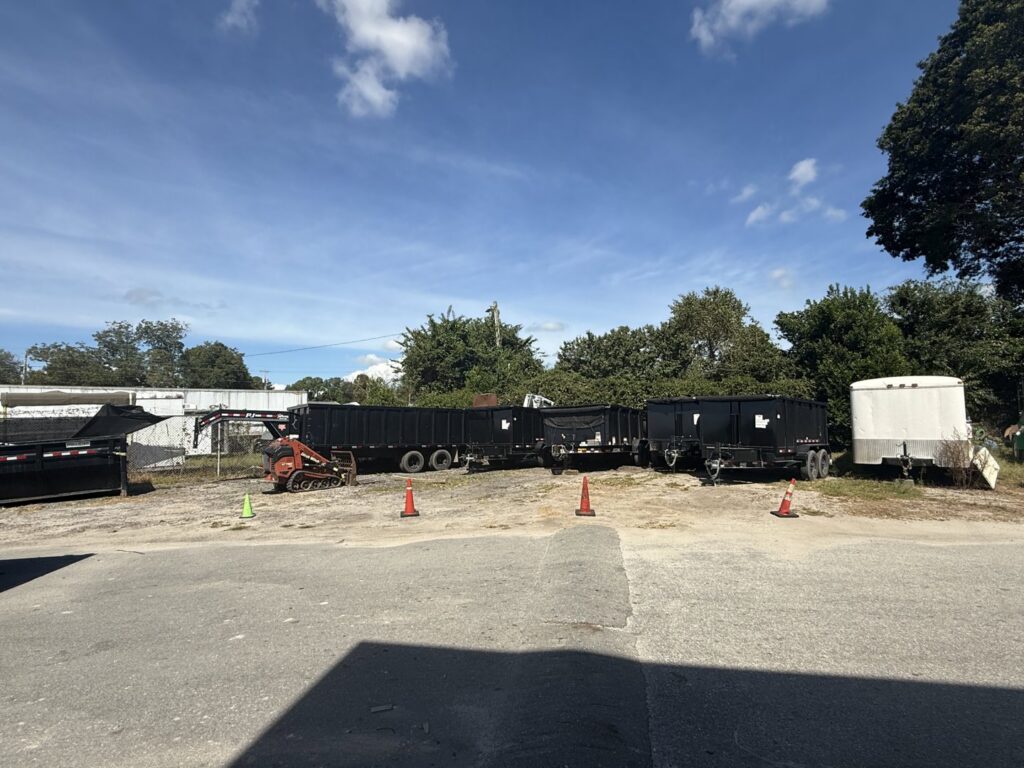 A fleet of SmartDumps black dump trailers and a skid steer parked in a lot, ready for junk removal services in Wilmington, NC.