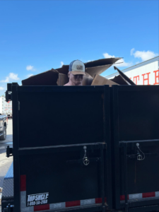 A SmartDumps black dump trailer filled with various junk items, including cardboard and a mannequin head, in Wilmington, NC.