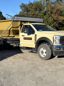 A light yellow SmartDumps junk removal truck parked on a sunny day in Wilmington, NC.