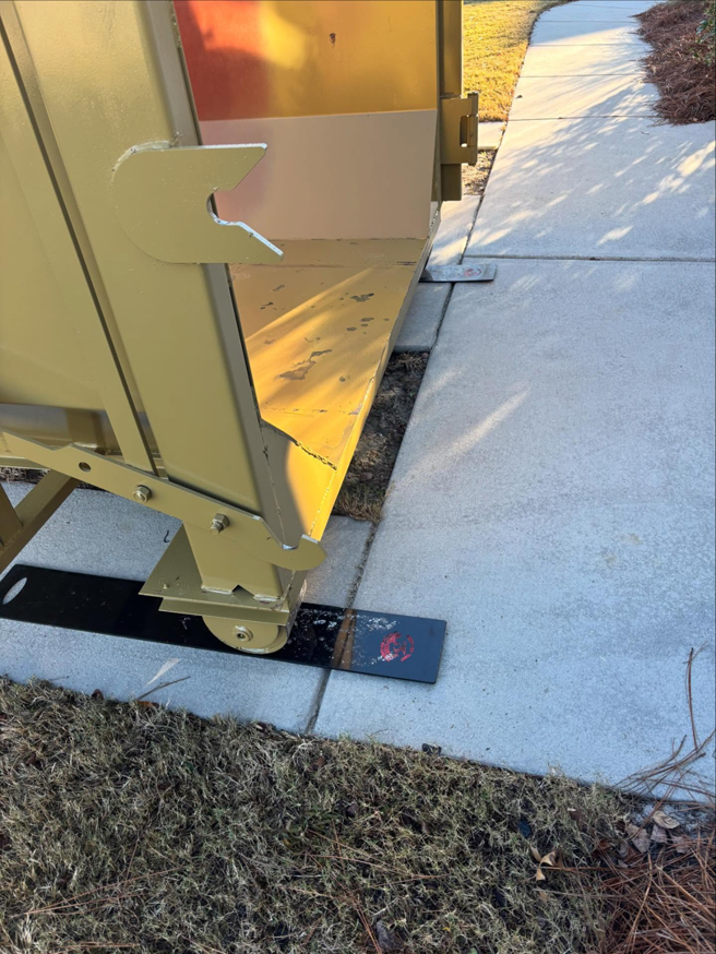 Close-up of a SmartDumps yellow roll-off dumpster base with protective pads on a concrete driveway in Wilmington, NC.