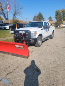 A white pickup truck equipped with a red snow plow, ready for snow removal services by 24/7 Snow Removal & Salting in Indianapolis, IN.
