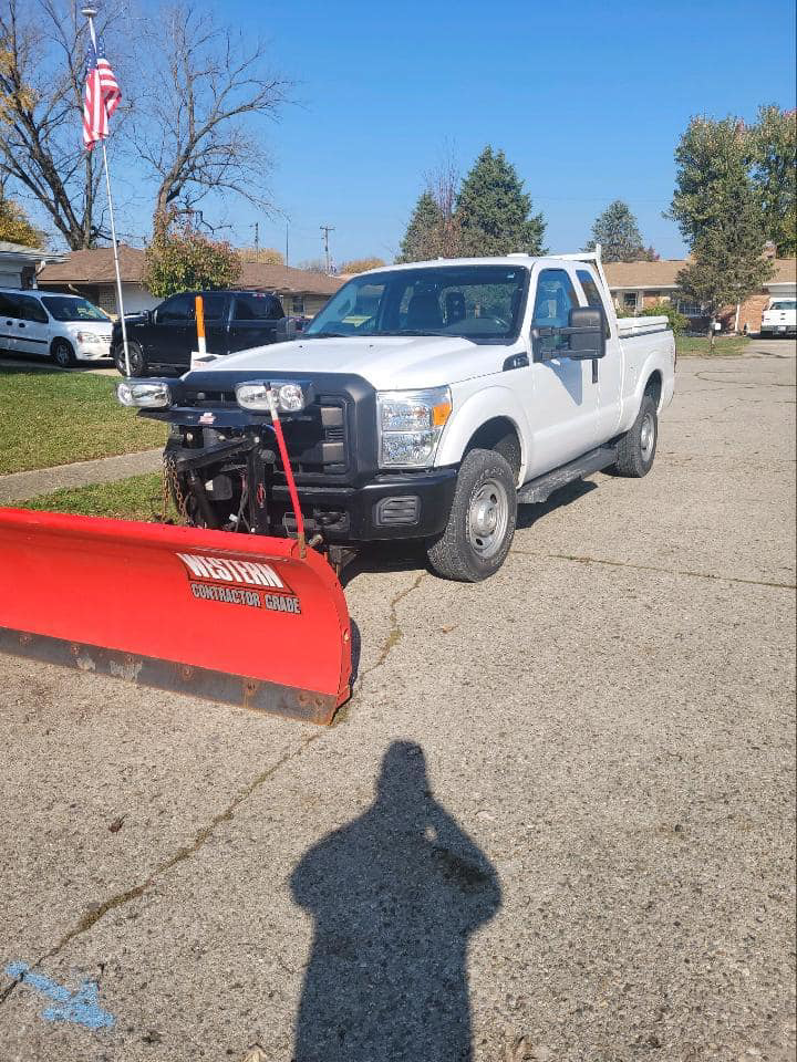 A white pickup truck equipped with a red snow plow, ready for snow removal services by 24/7 Snow Removal & Salting in Indianapolis, IN.