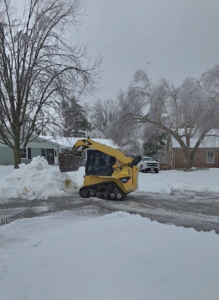A yellow skid steer loader performing snow removal services for Luv-2-Build, LLC in Lexington, KY.