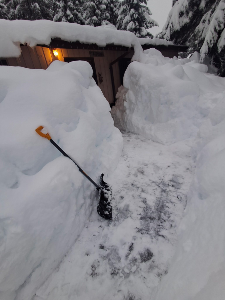A snow shovel leaning against a pile of snow next to a cleared path by Palma Construction in Paramus, NJ.