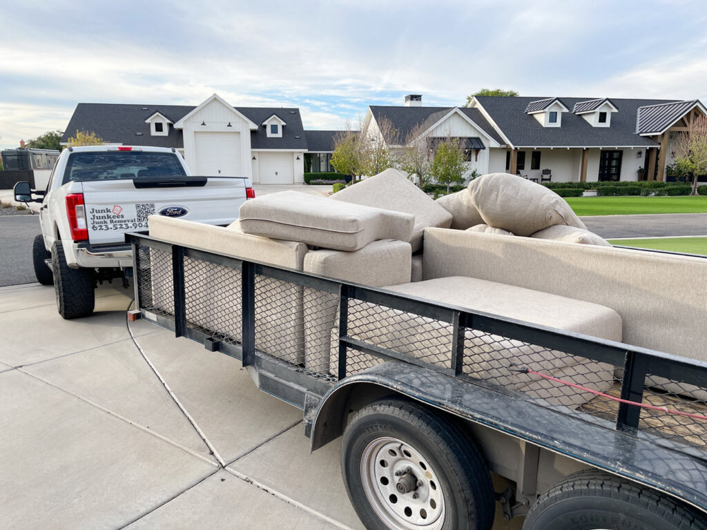 A Junk Junkees truck and trailer loaded with sofa cushions and furniture pieces for removal in Peoria, AZ.