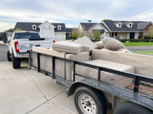 A Junk Junkees truck and trailer loaded with sofa cushions and furniture pieces for removal in Peoria, AZ.