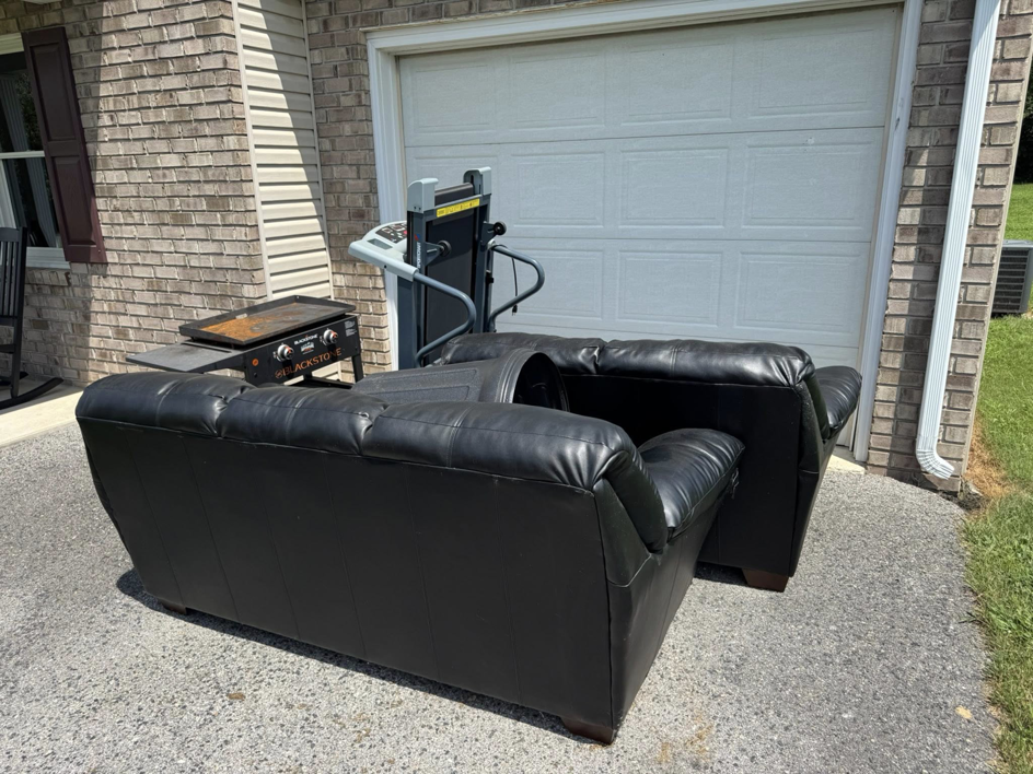 A black sofa, grill, and treadmill placed outside a garage for junk removal by Quick Lift Junk Removal in Hagerstown, MD.