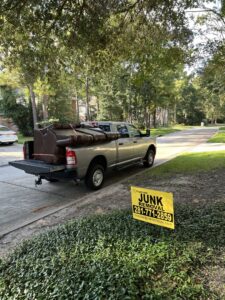 A large sofa secured in the bed of a pickup truck, with a 'Junk Removal' sign nearby, by Tidy Loaders Junk Removal in Houston, TX.