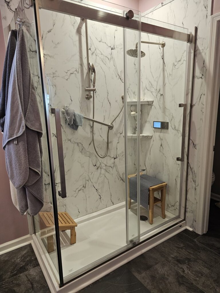 A spacious and accessible shower renovation with marble-look panels, grab bars, and a built-in bench by Peninsula Bath & Tile in Salisbury, MD.