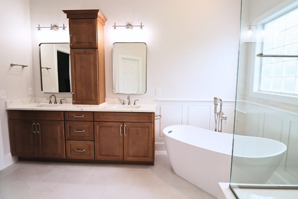 A spacious bathroom remodel with a double vanity, tall storage cabinet, freestanding tub, and glass shower enclosure by The Bath Shop in Raleigh, NC.